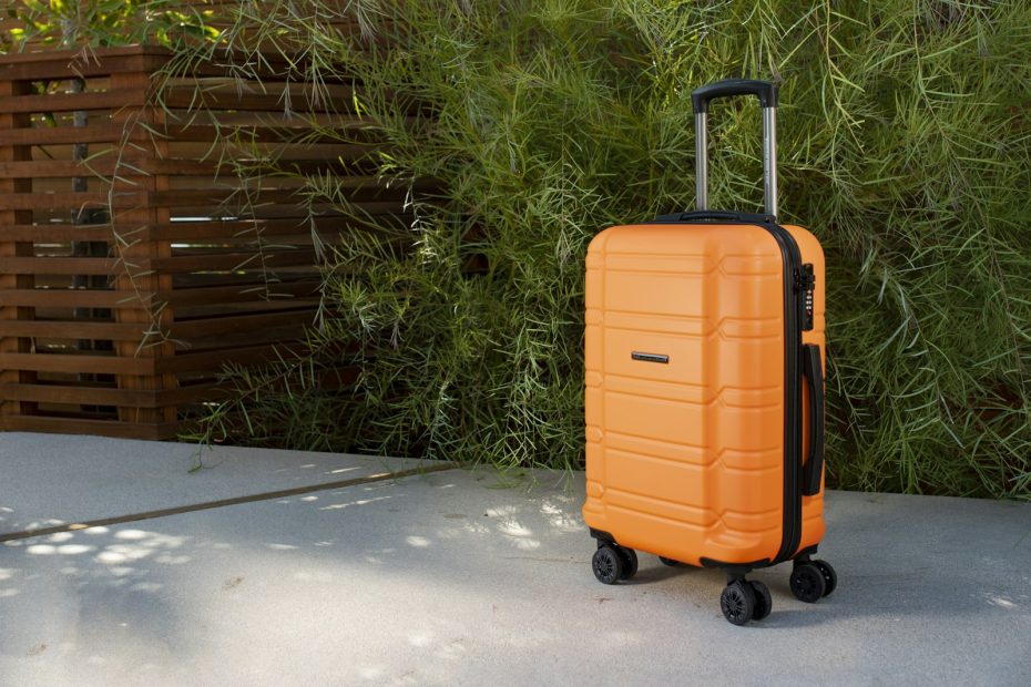 An orange carry-on suitcase on a sidewalk
