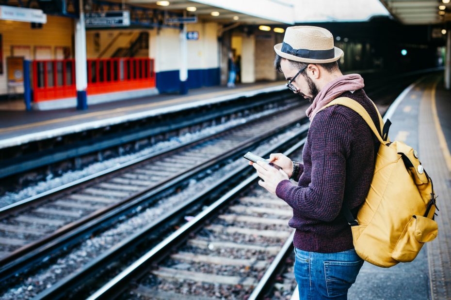 A traveler with a backpack using a phone on a train platform