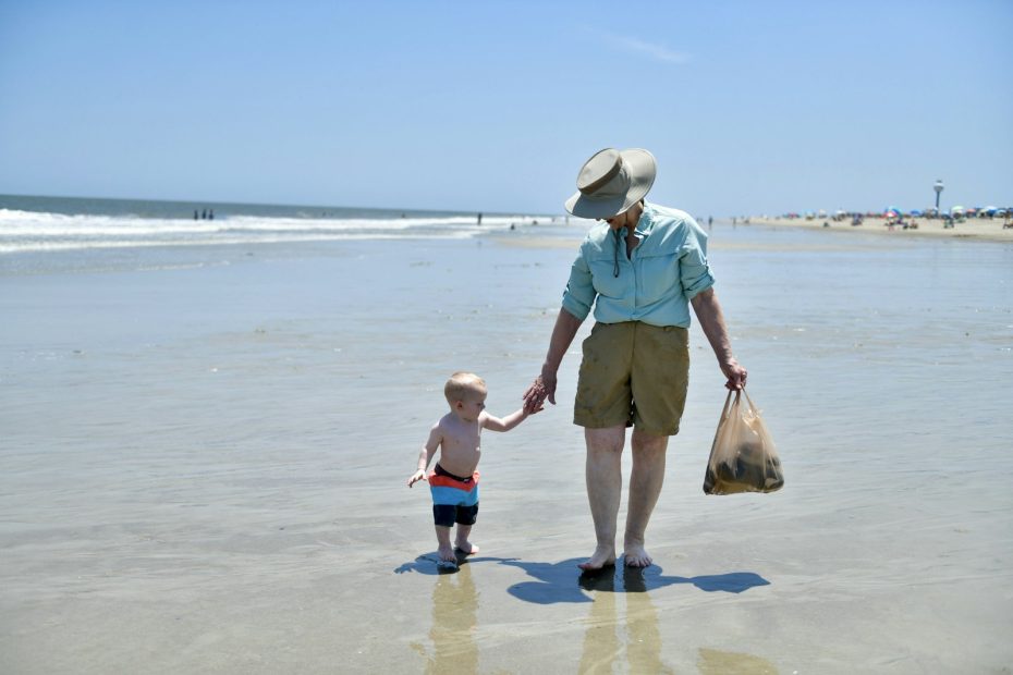 A grandparent and a young child walking hand in hand along the shore
