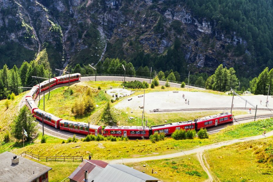 A red train curving through green alpine valleys