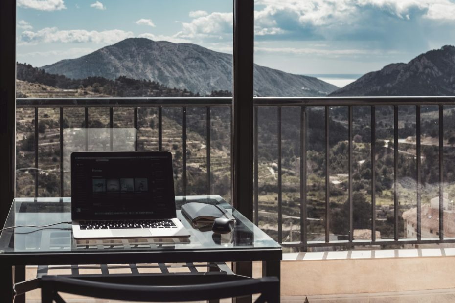 A laptop on a balcony table with mountains in the distance